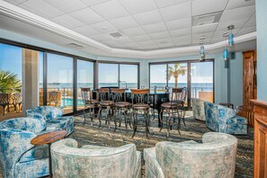 A spacious lounge area with a view of the ocean, featuring leather chairs, a wooden table, and a patterned carpet.