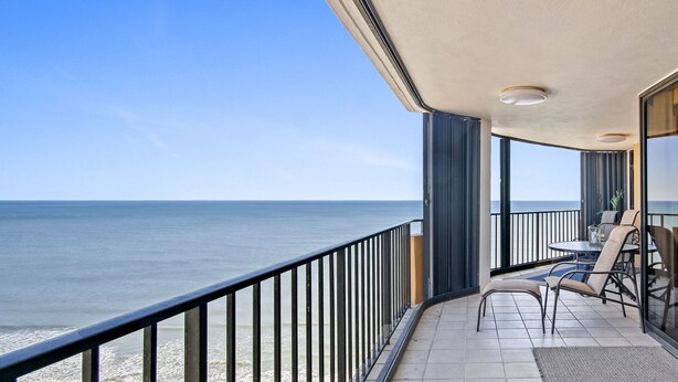 Een balkon met uitzicht op zee, een tafel met stoelen en een glazen balustrade.