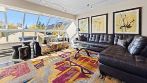 Un salon moderne avec une grande fenêtre, un canapé en cuir, une table basse en verre et un tapis coloré.