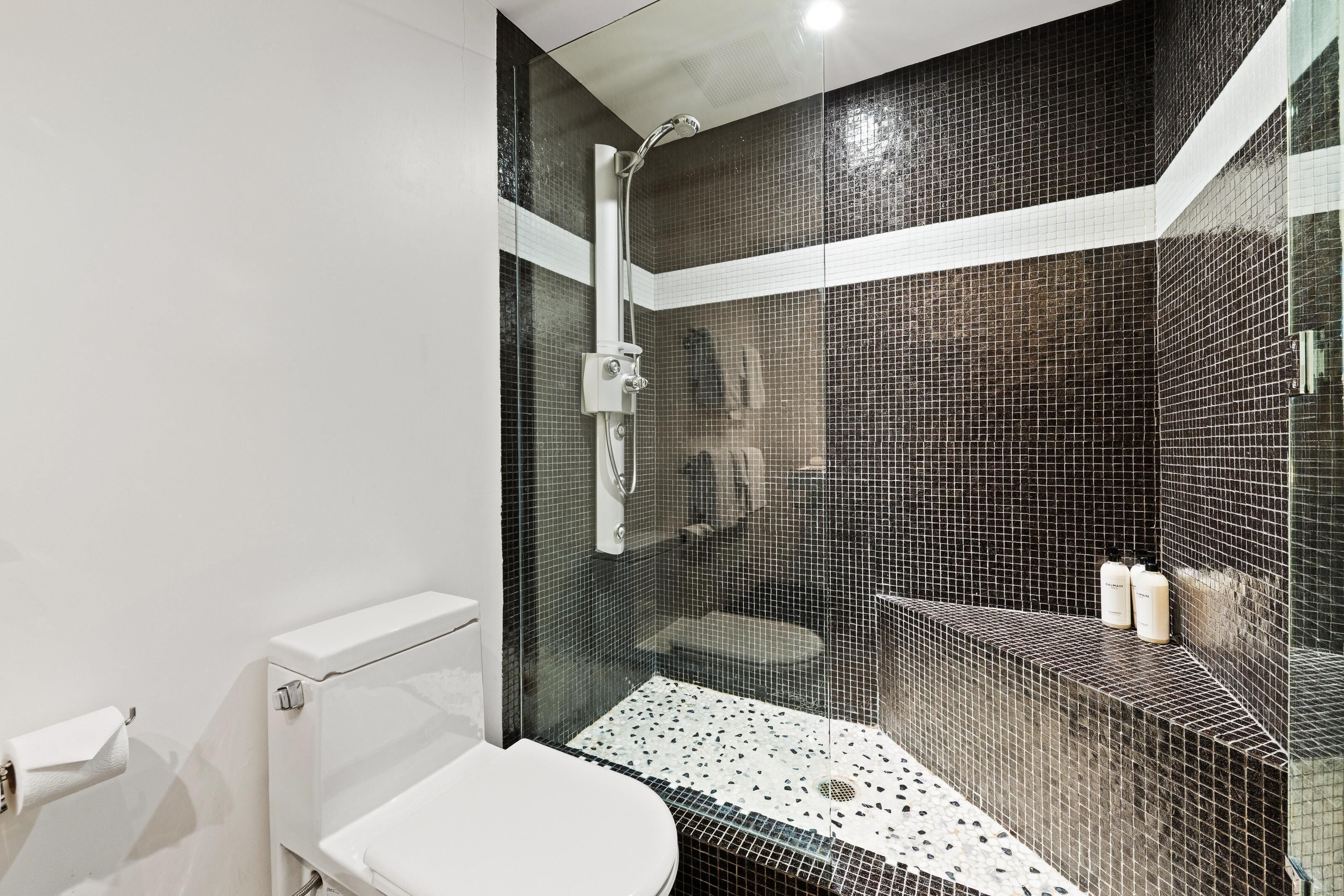 A modern bathroom with a glass-enclosed shower, a white toilet, and a tiled floor.