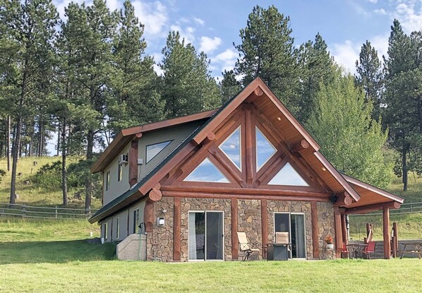 Situated in a serene landscape, this lodge features a large patio area with outdoor seating and a gable roof.
