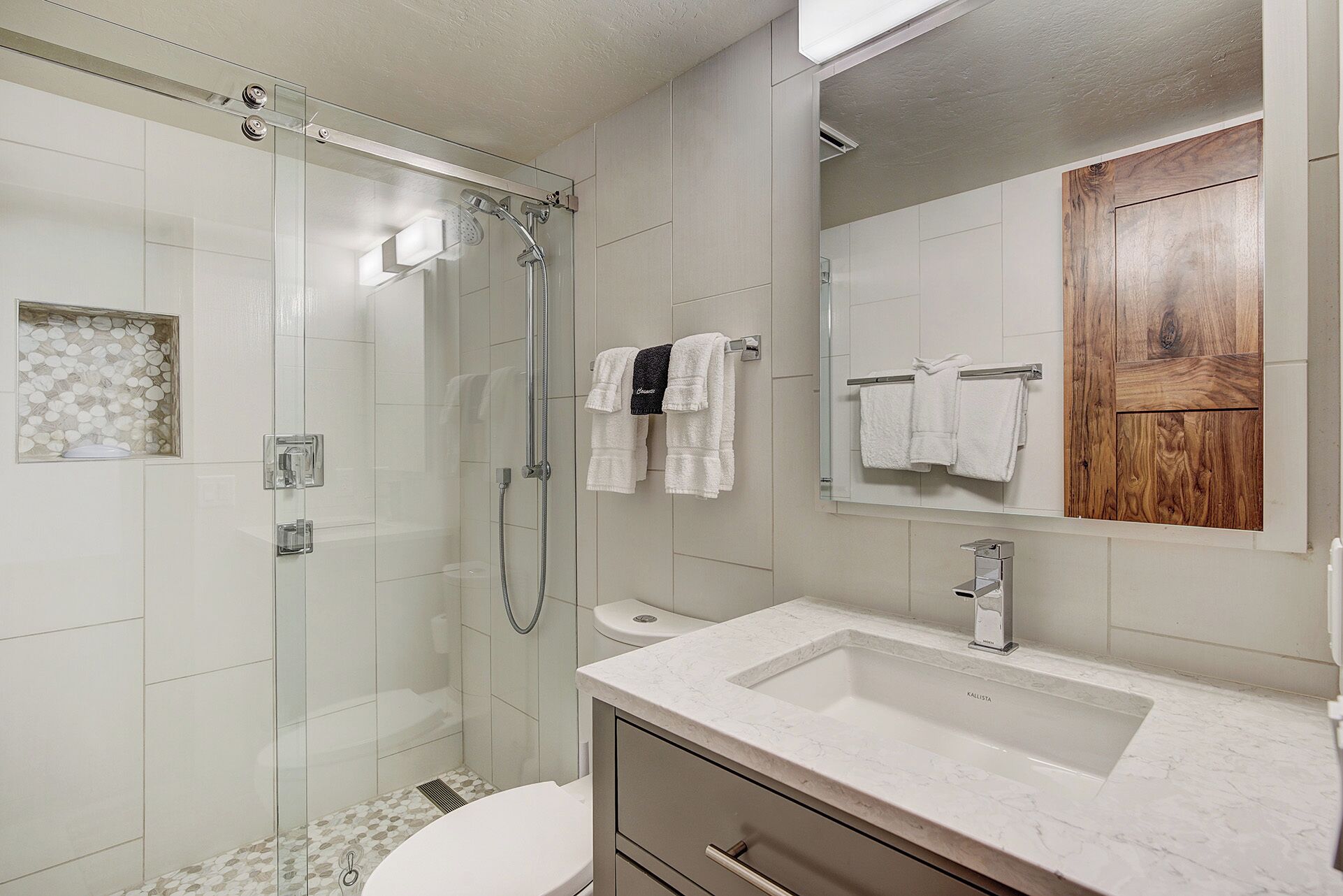 A modern bathroom with a glass-enclosed shower, a white sink, and a wooden door.