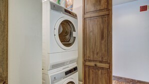 Un espace buanderie équipé d’un lave-linge et d’un sèche-linge superposés, de meubles en bois et d’un sol carrelé.