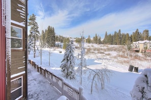 Un paisaje nevado con una terraza de madera y vistas a un campo y árboles cubiertos de nieve.