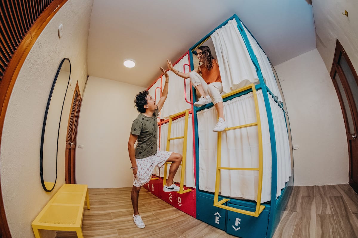 Een kamer met een stapelbed, een klein tafeltje en een houten bank.