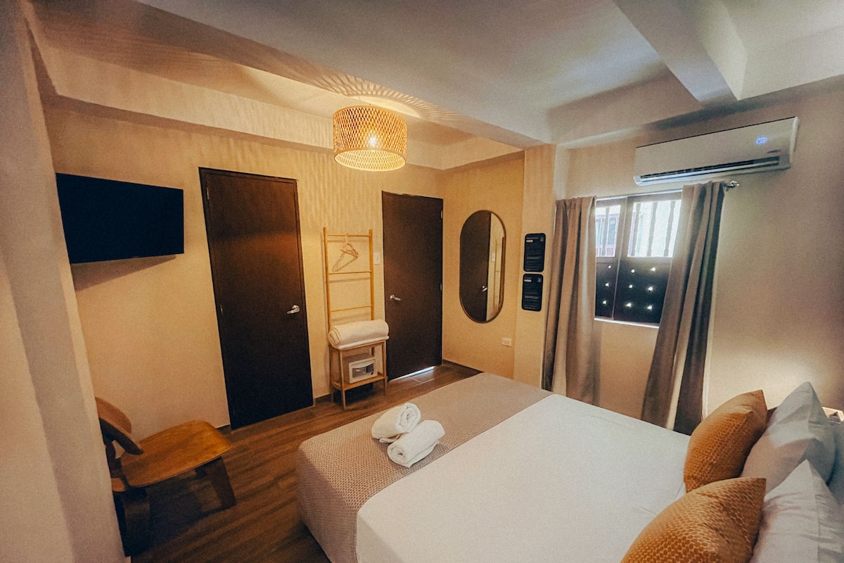 Hotelkamer met een groot bed, een houten vloer, een plafondlamp, een wandairconditioner en een raam met gordijnen.