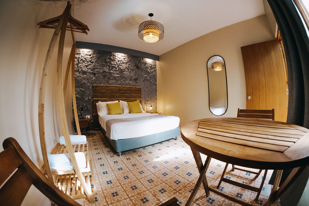Een slaapkamer met een bed, een houten tafel, een stoel, een spiegel en een hanglamp.