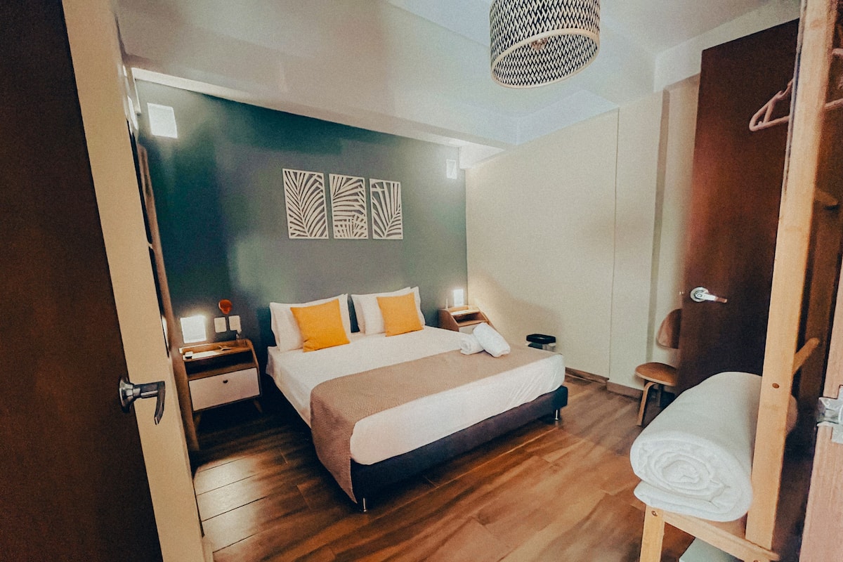 Een slaapkamer met een bed, nachtkastjes, een houten vloer, een kledingkast en een hanglamp.