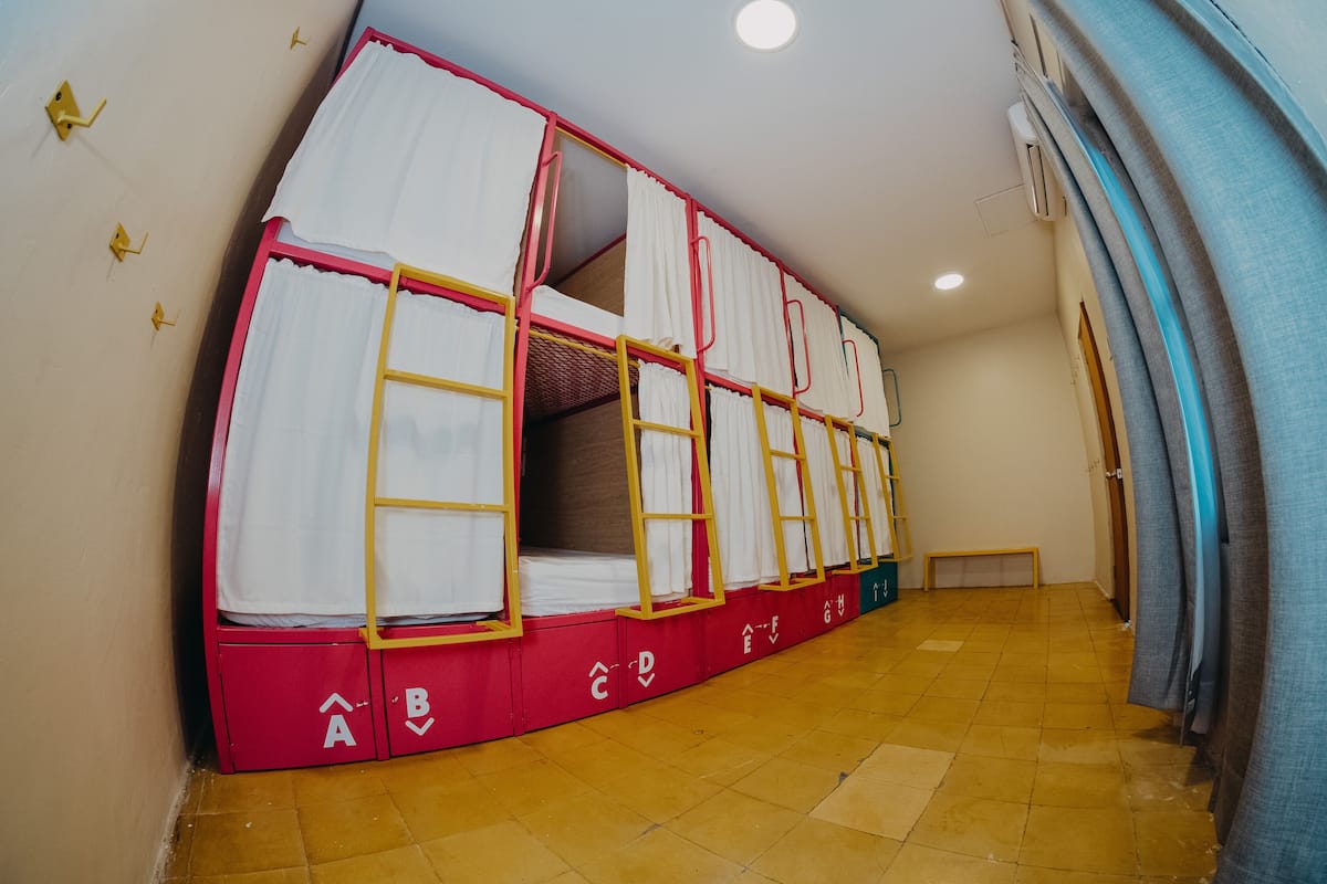 Een stapelbed met een ladder, witte gordijnen en een betegelde vloer.