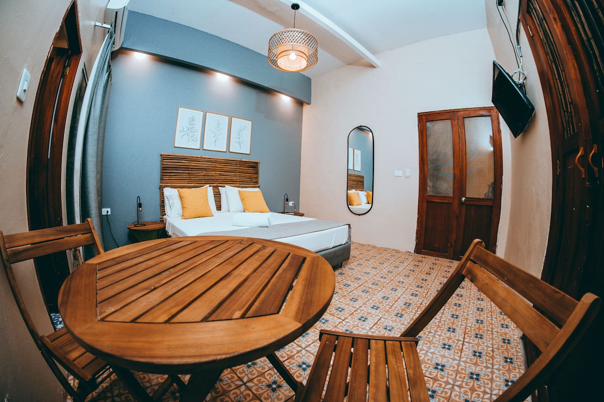 Een slaapkamer met een bed, nachtkastje en een ronde houten tafel met stoelen.