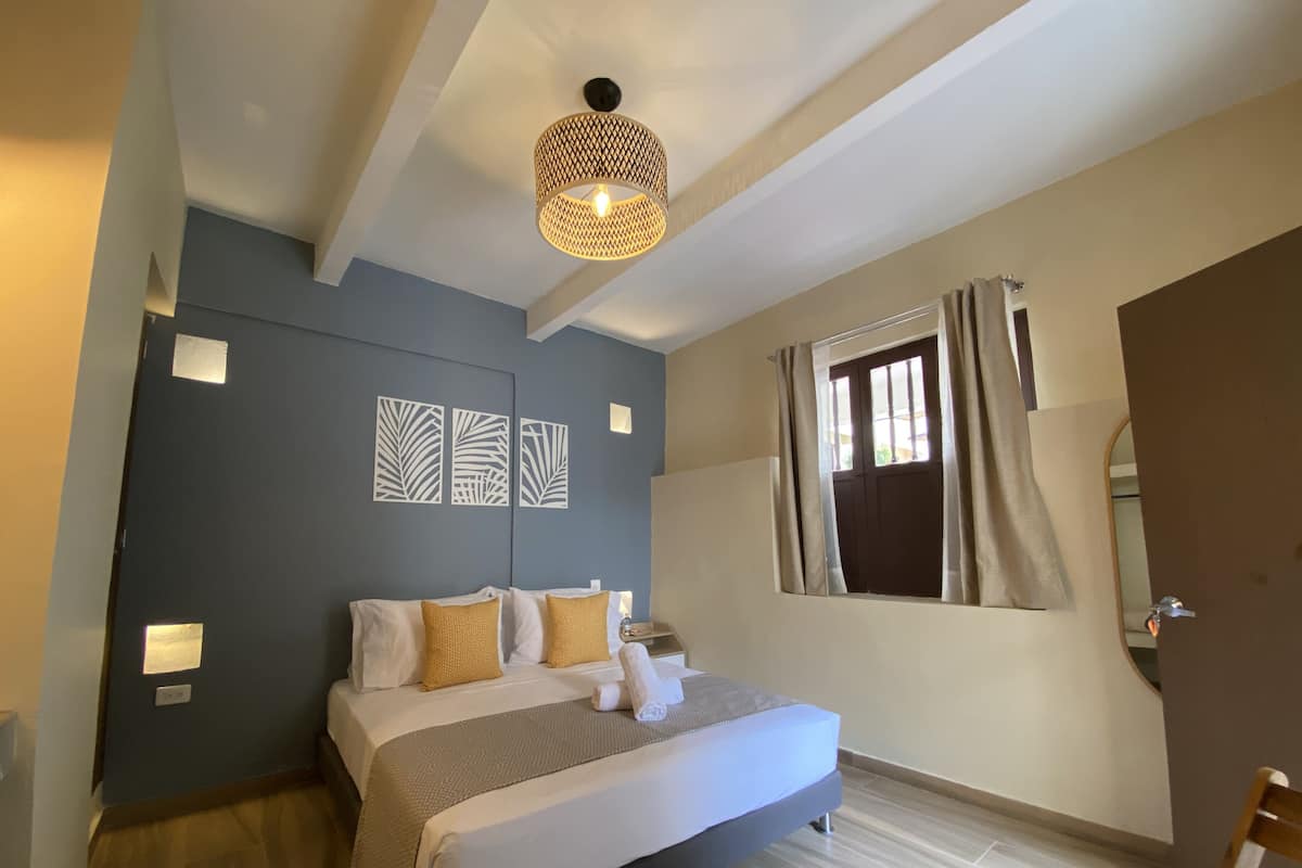 Een slaapkamer met een bed, een hanglamp, een raam met gordijnen en wanddecoratie.