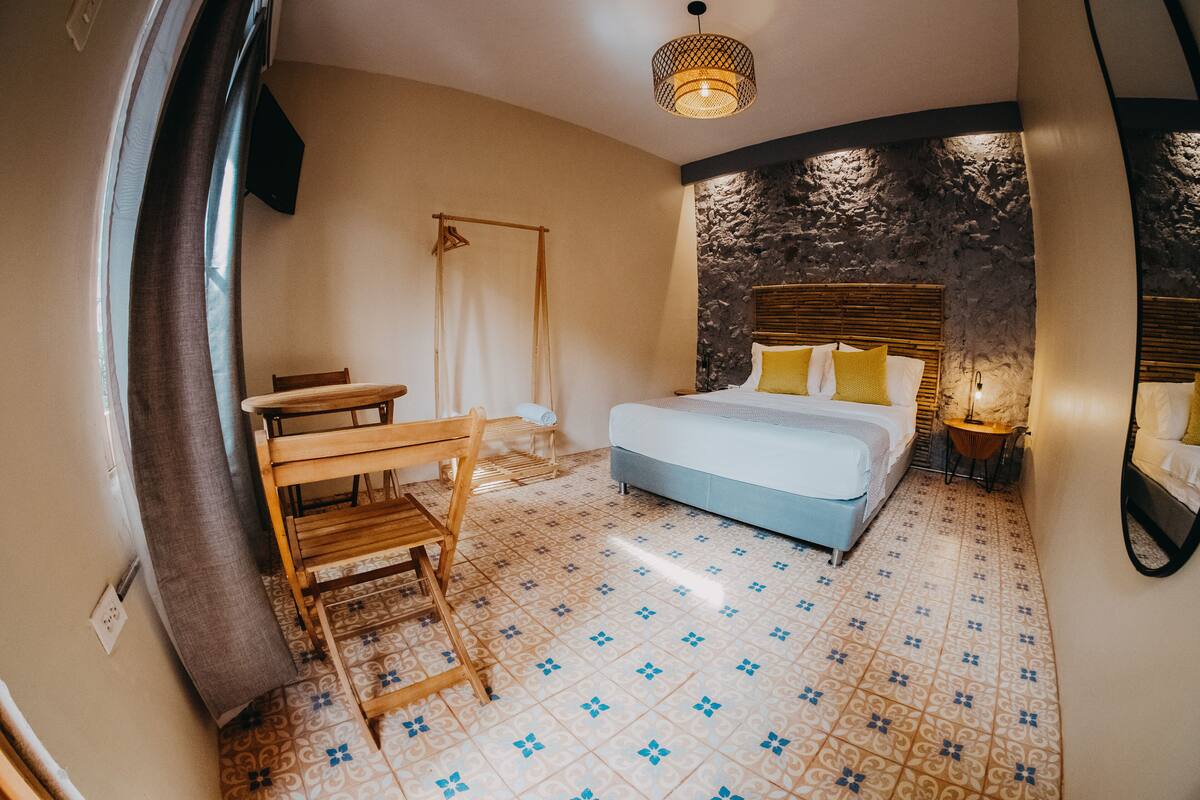 Een slaapkamer met een bed, een houten stoel, een kleine tafel, een hanglamp en een accentmuur van steen.