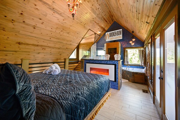 Una cabaña con interior de madera, una cama con cubrecama acolchado, una chimenea y un letrero que dice "BROKEN BOW CABIN LODGING".