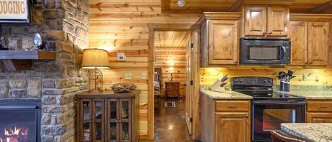 A cozy cabin-style kitchen with wooden cabinets, a stone fireplace, and a stone wall.