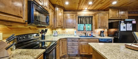 Une cuisine avec des armoires en bois, des comptoirs en granit, des appareils électroménagers en acier inoxydable et un tapis rouge.