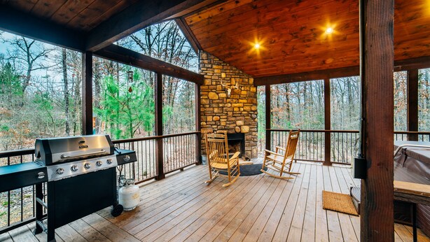 Een chalet met een stenen open haard, een barbecue en een terras met stoelen.
