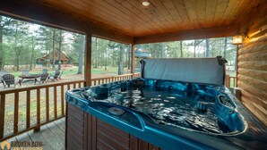 Un jacuzzi en una terraza de madera con vista a una cabaña y árboles.