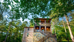 A two-story stone cabin with a wooden balcony and a stone staircase.