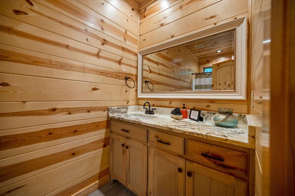 Baño de cabaña de madera con encimera de mármol, armarios de madera y un espejo sobre el lavamanos.