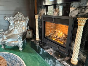 Une cheminée dont l’intérieur est en briques, flanquée de colonnes richement décorées et d’un fauteuil luxueux.