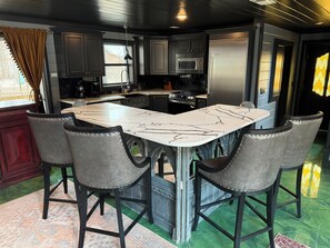 Une cuisine moderne dotée d’un îlot central, de meubles de couleur sombre, d’appareils électroménagers en acier inoxydable et d’un tapis au motif original.