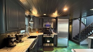 Eine kompakte Küche mit dunklen Schränken, einem Edelstahl-Kühlschrank, einer Mikrowelle und einem Backofen.