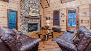 L’intérieur d’un chalet confortable, avec des murs en rondins de bois, une cheminée en pierre, des canapés en cuir et une enseigne sur laquelle on peut lire « BROKEN BOW ».
