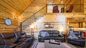 Ein Holzblockhaus-Interieur mit einem Wohnbereich, ausgestattet mit Ledersofas, einem Couchtisch und einer Treppe zu einer Schlafgalerie.