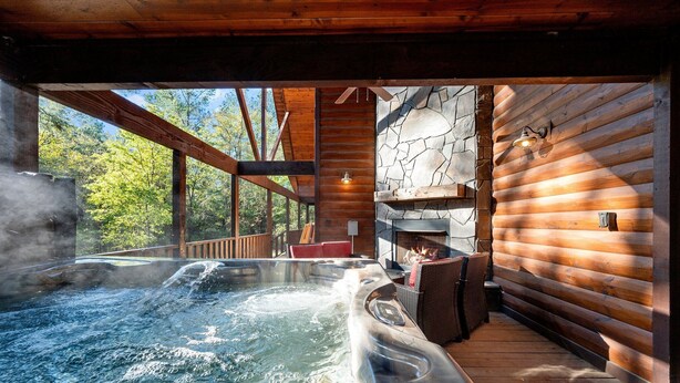 Ein Whirlpool mit Holzterrasse, Steinwand und Kamin.