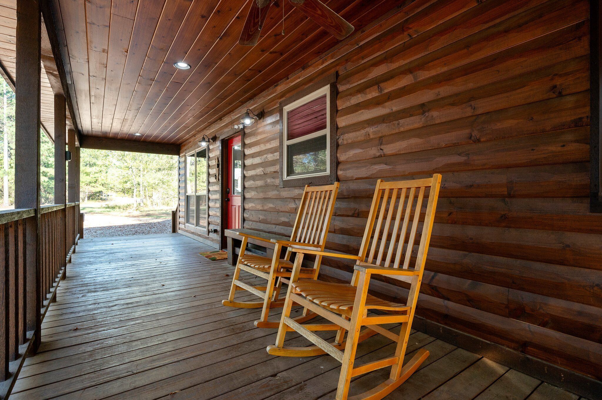 Une véranda en bois avec des fauteuils à bascule et une terrasse en bois.