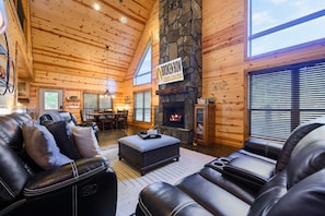 Ein gemütliches Interieur im Chalet-Stil mit Ledersofas, einem Kamin aus Stein und Holzwänden.