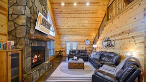 Ein gemütliches Interieur im Chalet-Stil mit Kamin aus Stein, Ledersofas und Holzbalkendecke.