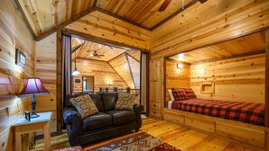 A cozy cabin interior with a leather sofa, a bed with a checkered blanket, and a patterned rug.