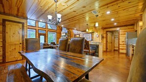 A wooden interior with a large dining table, chairs, and a kitchen area.