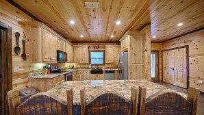A wooden cabin-style kitchen with granite countertops, wooden cabinets, and a dining area with a large table and chairs. - Caddy Shack | Luxury Group Lodge Near Broken Bow Lake with Game Room and Expansi (Broken Bow)