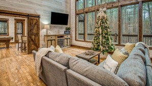 L’intérieur chaleureux d’un chalet avec une grande fenêtre, des murs en bois, une cheminée et un sapin de Noël.