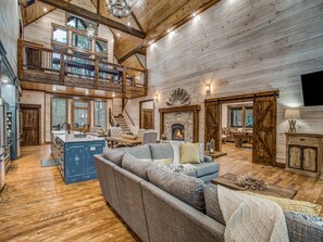 Ein großzügiger Wohnbereich mit hoher Decke, Holzdielenboden, Kamin und einer großen Couch.