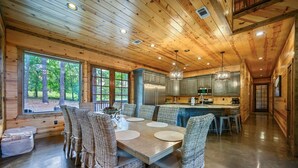 A wooden cabin interior with a dining area, kitchen, and large windows.