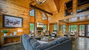 A spacious cabin with a stone fireplace, wooden walls, and large windows.