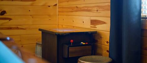 A wooden interior with a small table, a stool, and a clock on the wall.