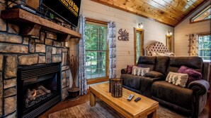 Un chalet confortable avec une cheminée, un canapé douillet et un téléviseur fixé au mur.