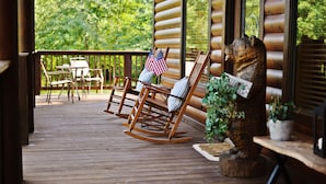A wooden deck with rocking chairs, a table, and American flags.