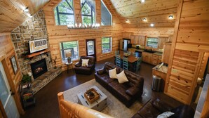 A log cabin interior with a stone fireplace, leather sofas, a dining area, and a kitchen.
