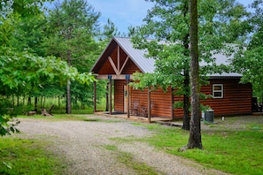 Situated in a lush forest, this cabin features a triangular roof and a cozy porch with benches.