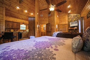 Cozy cabin-style room with a large bed, sofa, and dining area, featuring a kitchenette with a sink and refrigerator.