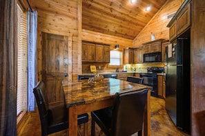 Kitchen features a central island, black refrigerator, microwave, and stove, along with wooden cabinets and a window.