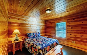 A cabin room with a bed, a nightstand, a lamp, and a window with blinds.