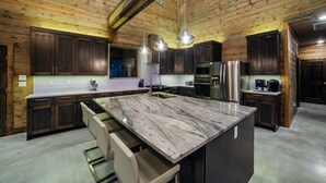 A modern kitchen with dark wood cabinets, a large marble island, stainless steel appliances, and pendant lighting.