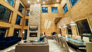 A cabin with a stone fireplace, wooden walls, and a dining area with chairs and a table.