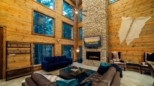 A cabin with a stone fireplace, a mounted TV, and a large window overlooking a forest.